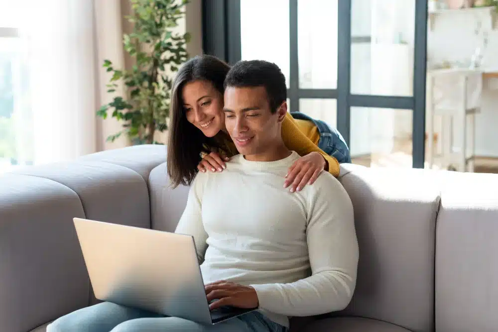 Pareja joven usando un ordenador portátil en casa, revisando la aprobación de préstamos de 2000 euros