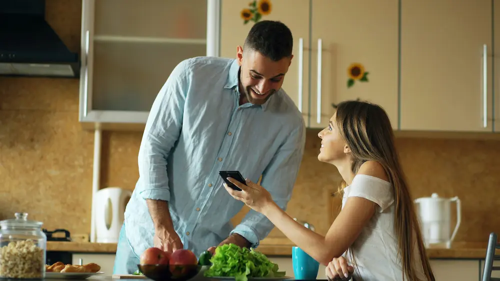 Pareja feliz en la cocina descubre en el móvil un préstamo rápido de 50 euros