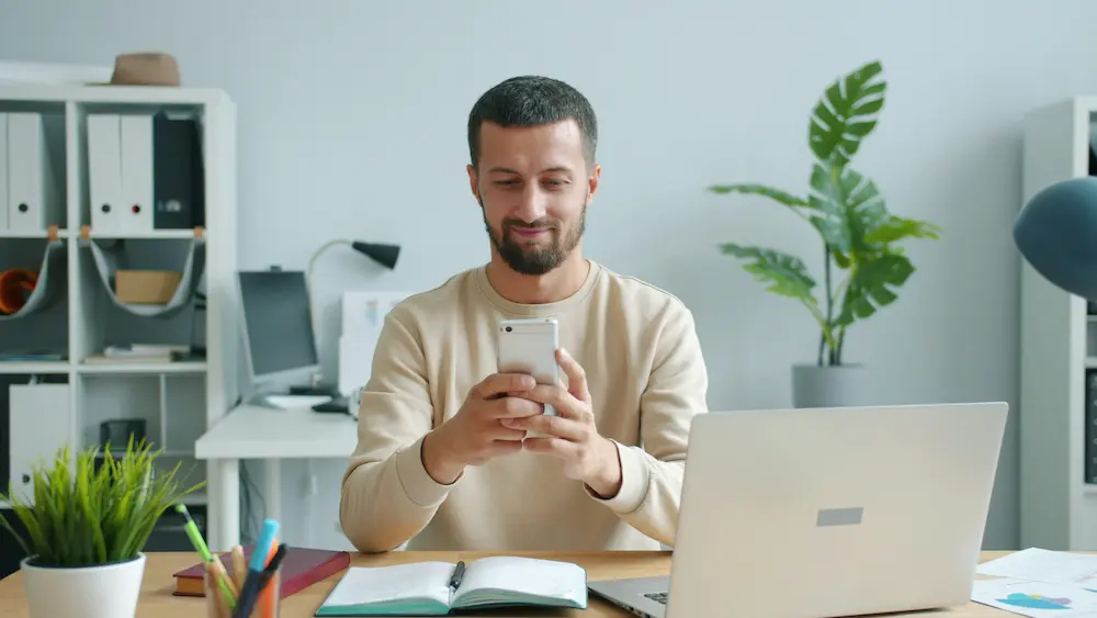 Hombre relajado sonríe mientras revisa en su móvil la aprobación de su microcrédito online de 50 euros