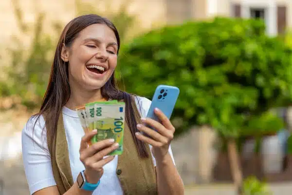Joven con dinero en efectivo y móvil, disfrutando de la rapidez de los préstamos de 7000 euros para estudios